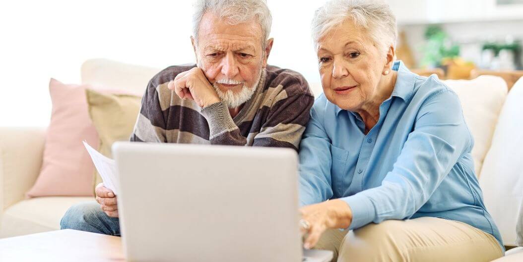 Elderly Couple Reviewing Documents on Laptop at Independent Living Facility