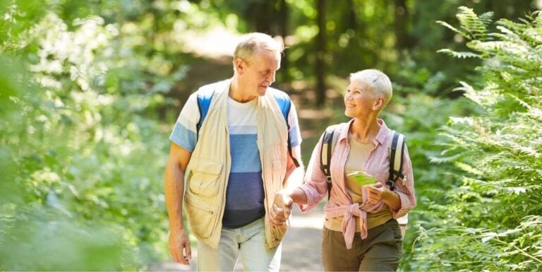 Elderly Couple Holding Hands Walking along a Wooded Nature Trail at Independent Living Facility