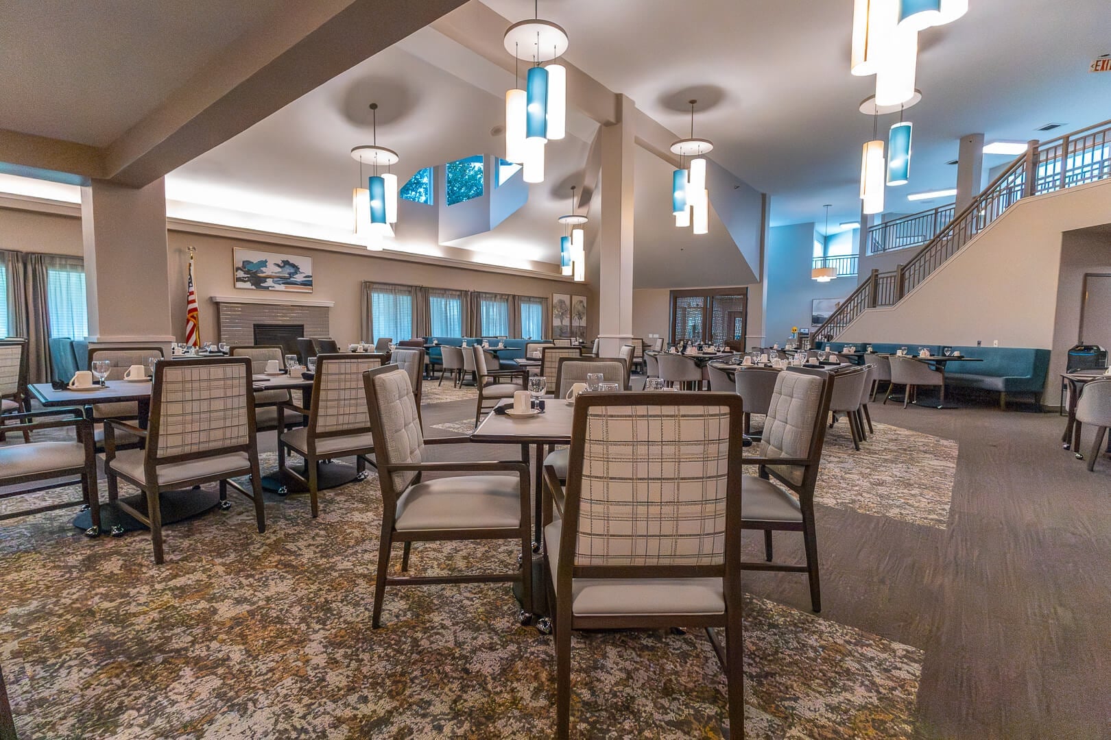Bright Two-Story Dining Hall with Pendant Lighting and Staircase at an Independent Living Facility